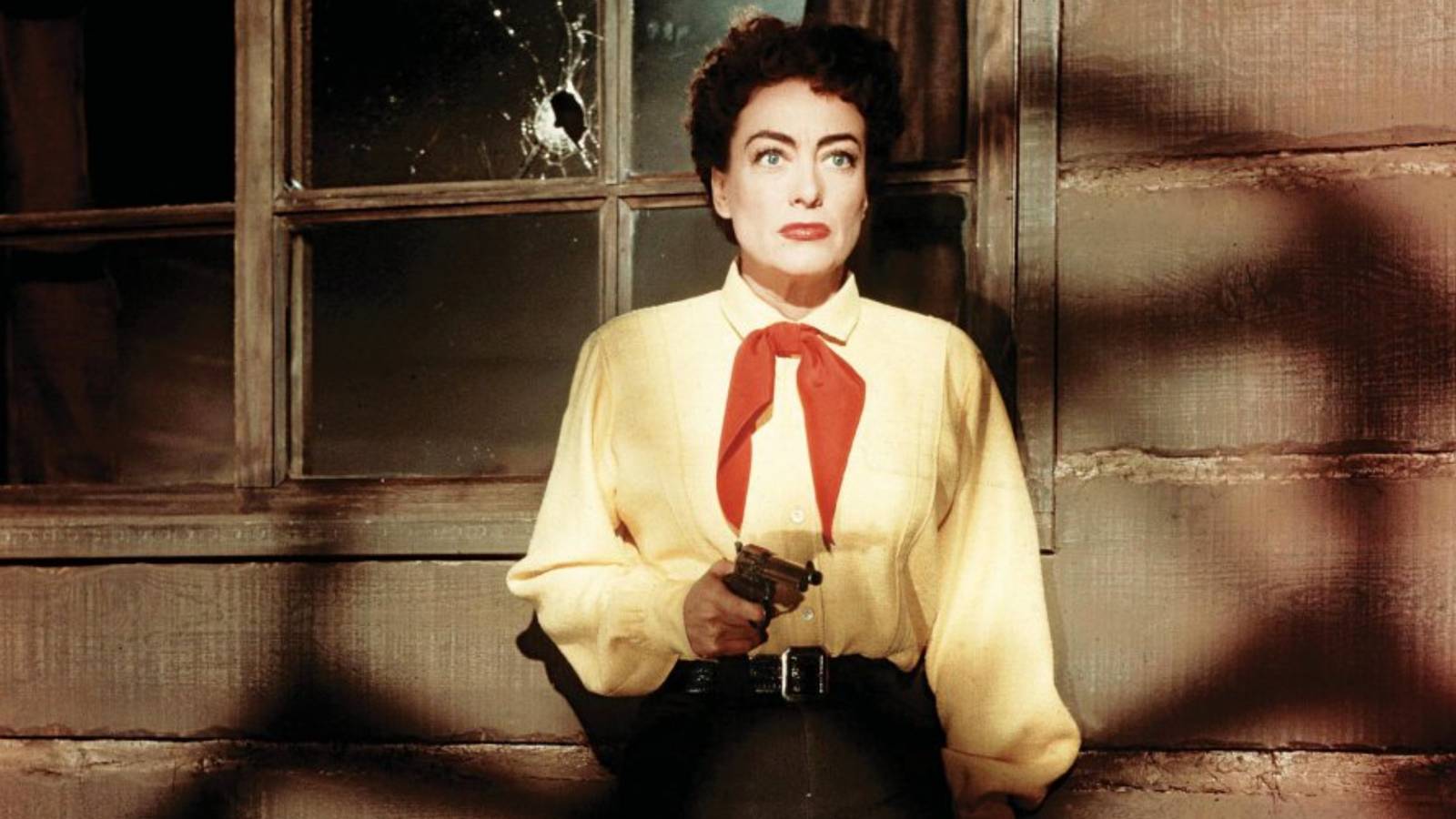 Vienna (Joan Crawford) stands in shadows with a yellow shirt aiming a revolver in 'Johnny Guitar'