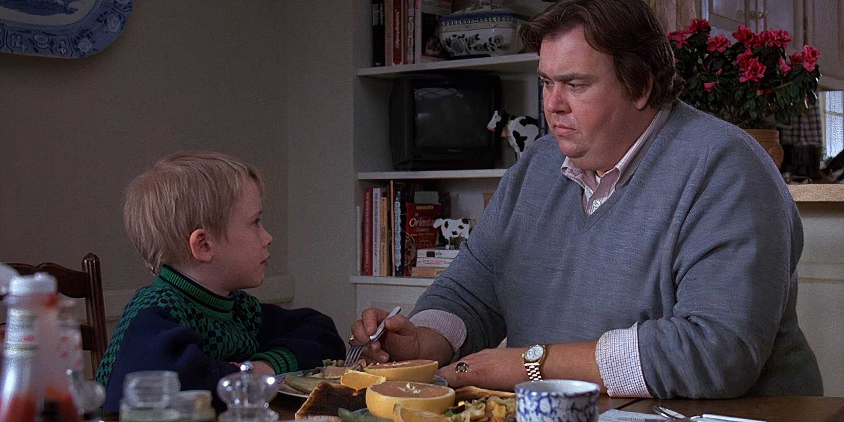 Macaulay Culkin sitting at a table looking at John Candy sitting next to him in Uncle Buck (1989).