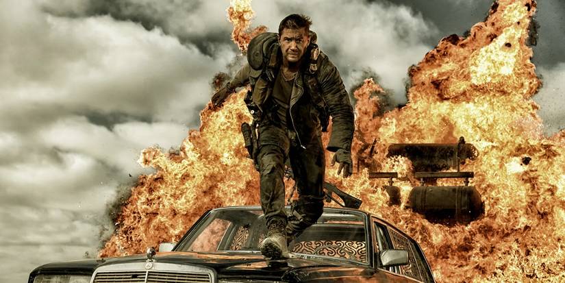 Max (Tom Hardy) on top of a car preparing to jump with an explosion behind him in Mad Max: Fury Road.