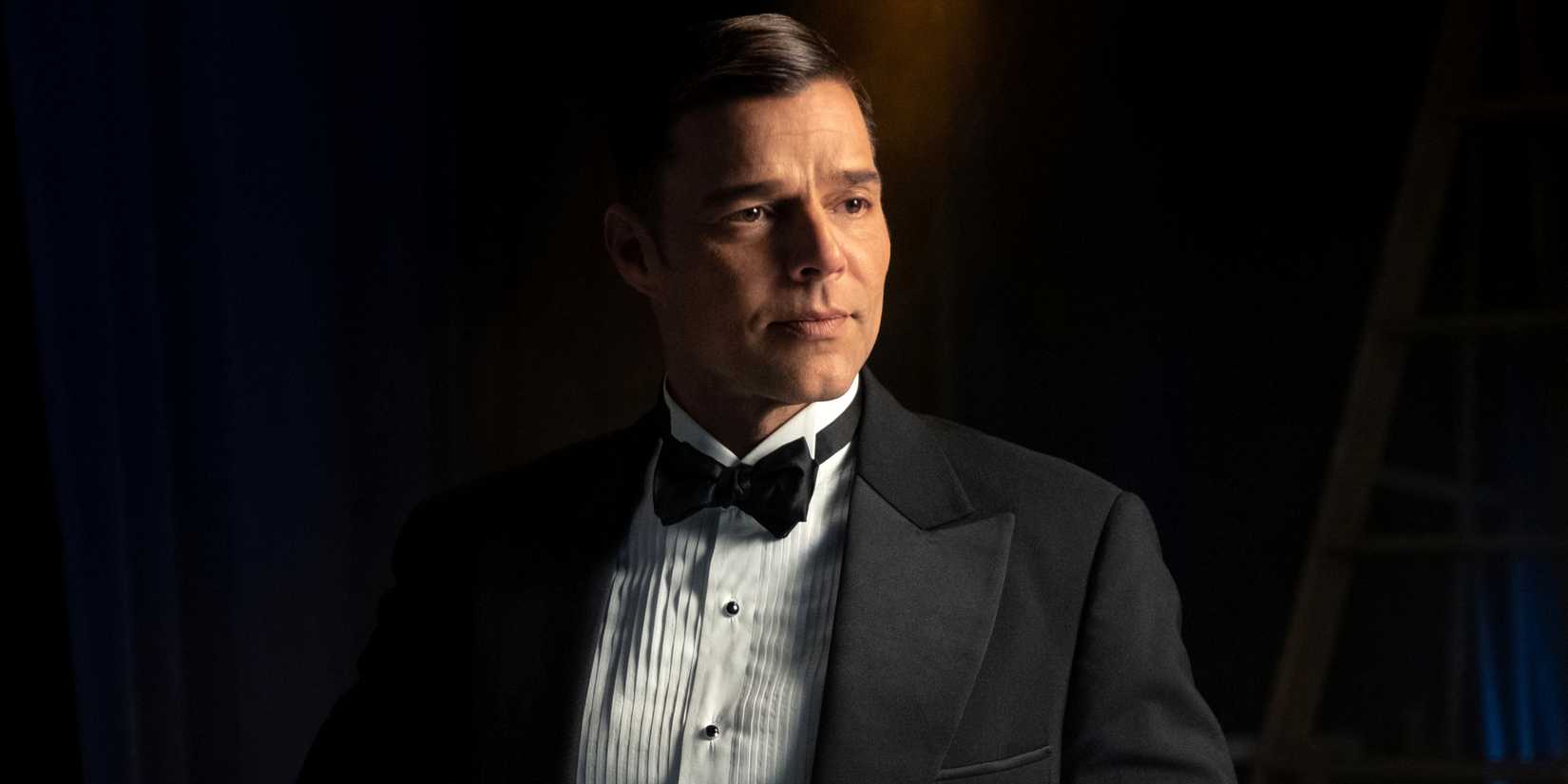 Ricky Martin as Robert Diaz in a tuxedo while standing in partial shadow in Episode 10 of Palm Royale