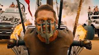 Max, played by Tom Hardy, strapped to the front of a vehicle with mask on in Mad Max: Fury Road (2015).