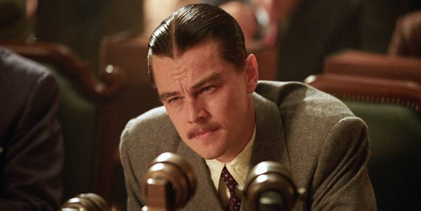 Leonardo Dicaprio as Howard Hughes in a hearing, sitting at a mic, in The Aviator