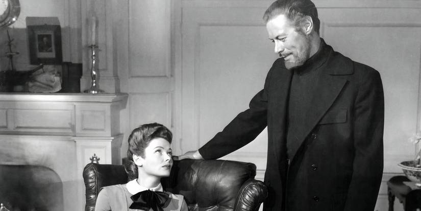 Lucy Muir (Gene Tierney) sitting in a chair and staring wistfully up at Daniel Cregg (Rex Harrison), who's standing by her chair with his hand resting on it and staring down at her with a smile in The Ghost and Mrs. Muir