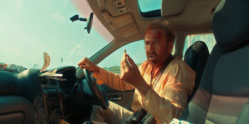 Nicolas Cage sits in a car holding up a bullet and looking panicked in The Surfer