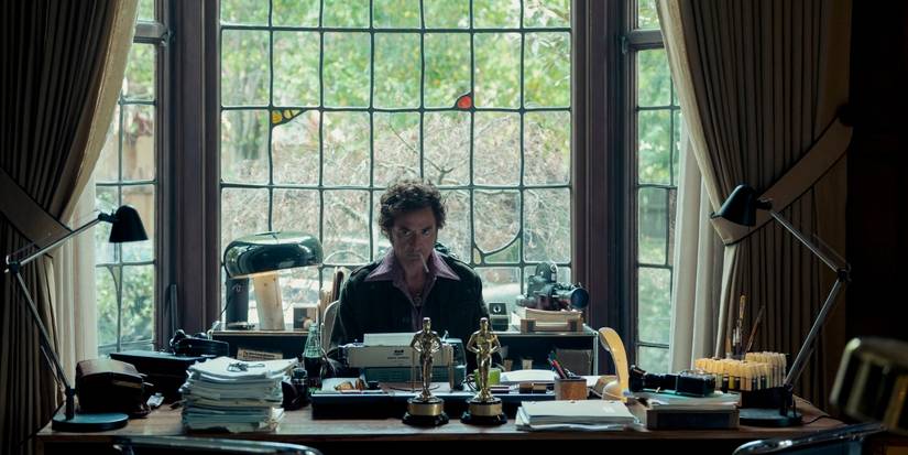 Robert Downey Jr. sitting at a desk with two Oscar statuettes in The Sympathizer Episode 4