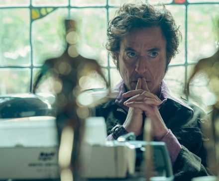 Robert Downey Jr. sitting at a desk with Oscars in the foreground in The Sympathizer Episode 4