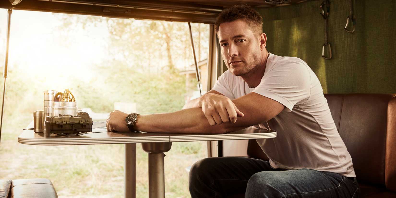 Justin Hartley as Colter Shaw sitting at a table in a white t-shirt and jeans in Season 1 of CBS' Tracker