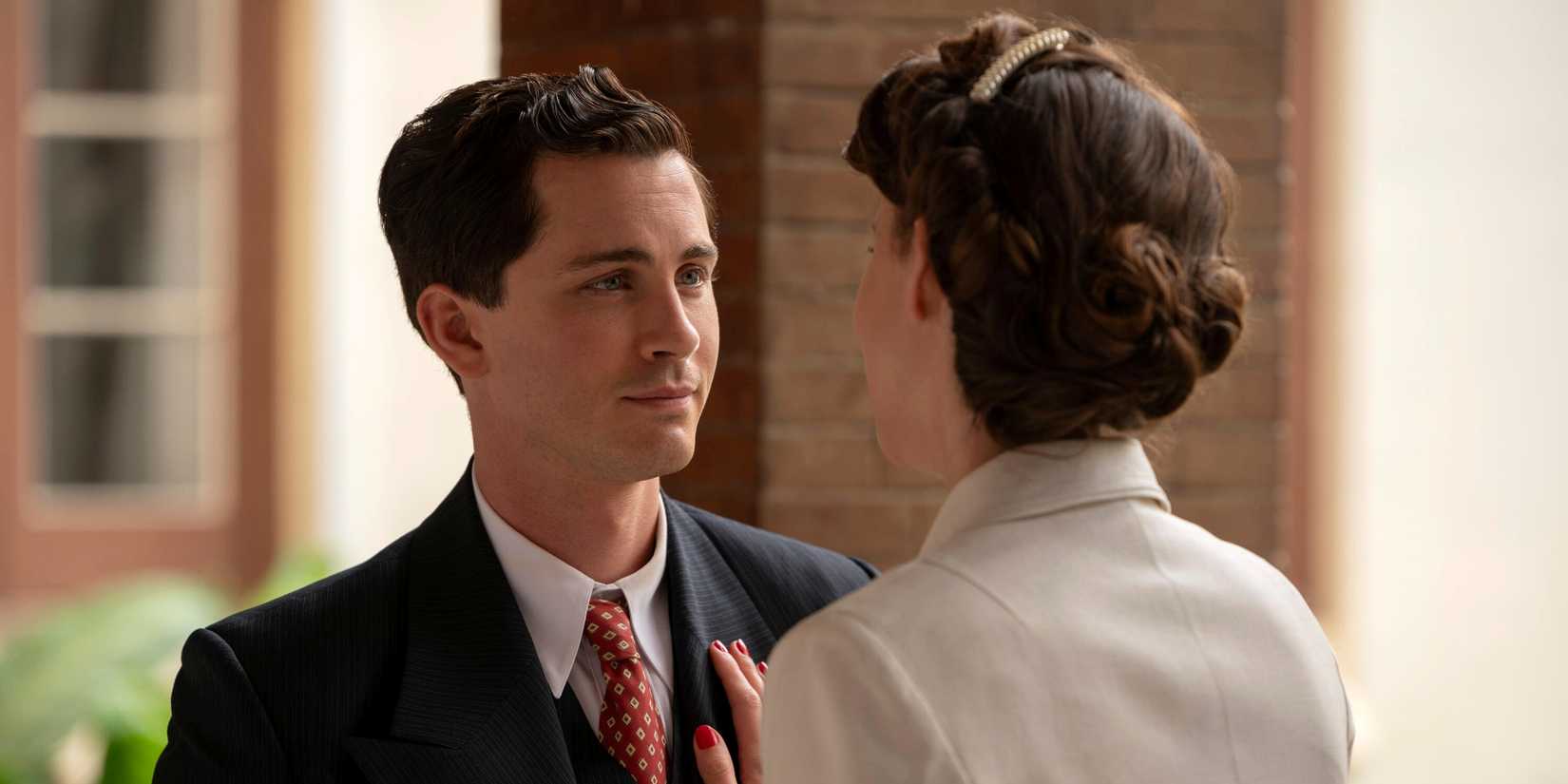 Logan Lerman as Addy Kurc in a suit and tie looking affectionately at a woman in We Were the Lucky Ones