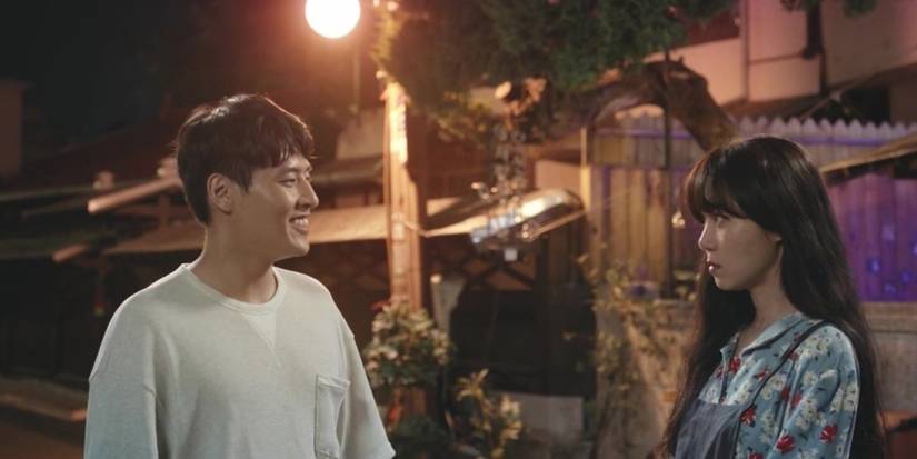 A man smiles while a woman stares seriously at him, standing outside at night in When the Camellia Blooms.