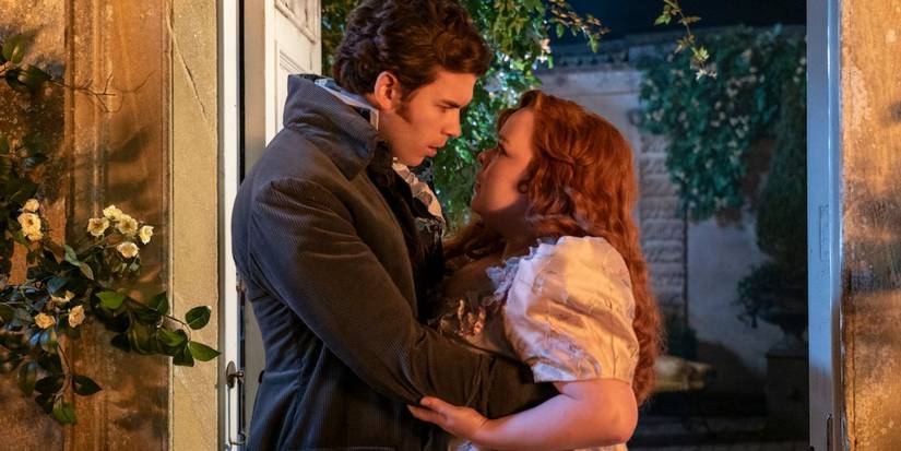 Colin and Penelope embrace each other in a garden. They are staring intensely at each other in Bridgerton.