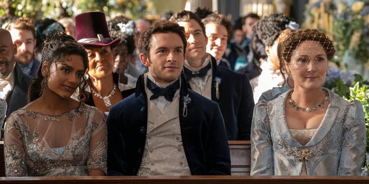 Simone Ashley, Jonathan Bailey, and Ruth Gemmell sitting in a church pew at Colin and Penelope's wedding