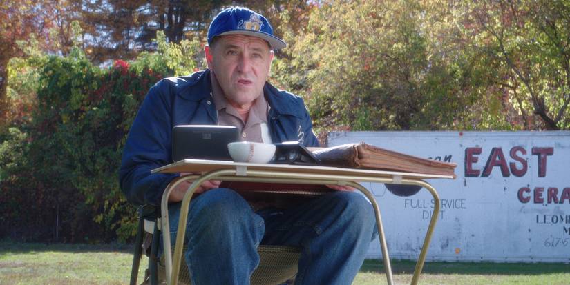 A man sits at a desk watching a baseball game in a still from Eephus. 