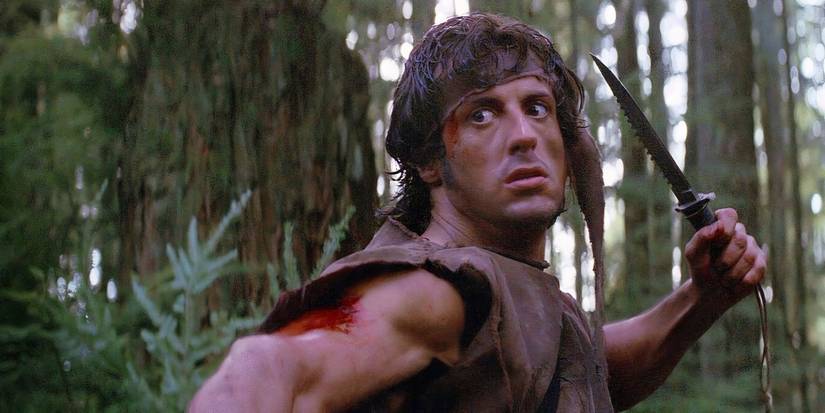 Sylvester Stallone as John Rambo posing with a hunting knife in the forest in 'First Blood.'