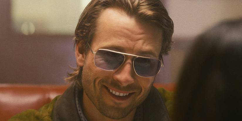 Glen Powell smiling and wearing Aviators at a diner in Richard Linklater's Hitman.