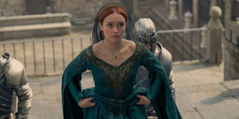 Alicent walks up steps, holding her gown looking worried, with 2 soldiers behind her in House of the Dragon