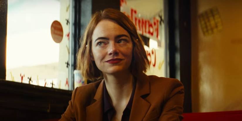 Emma Stone as Emily, smiling and sitting in a cafe in a still from 'Kinds of Kindness'