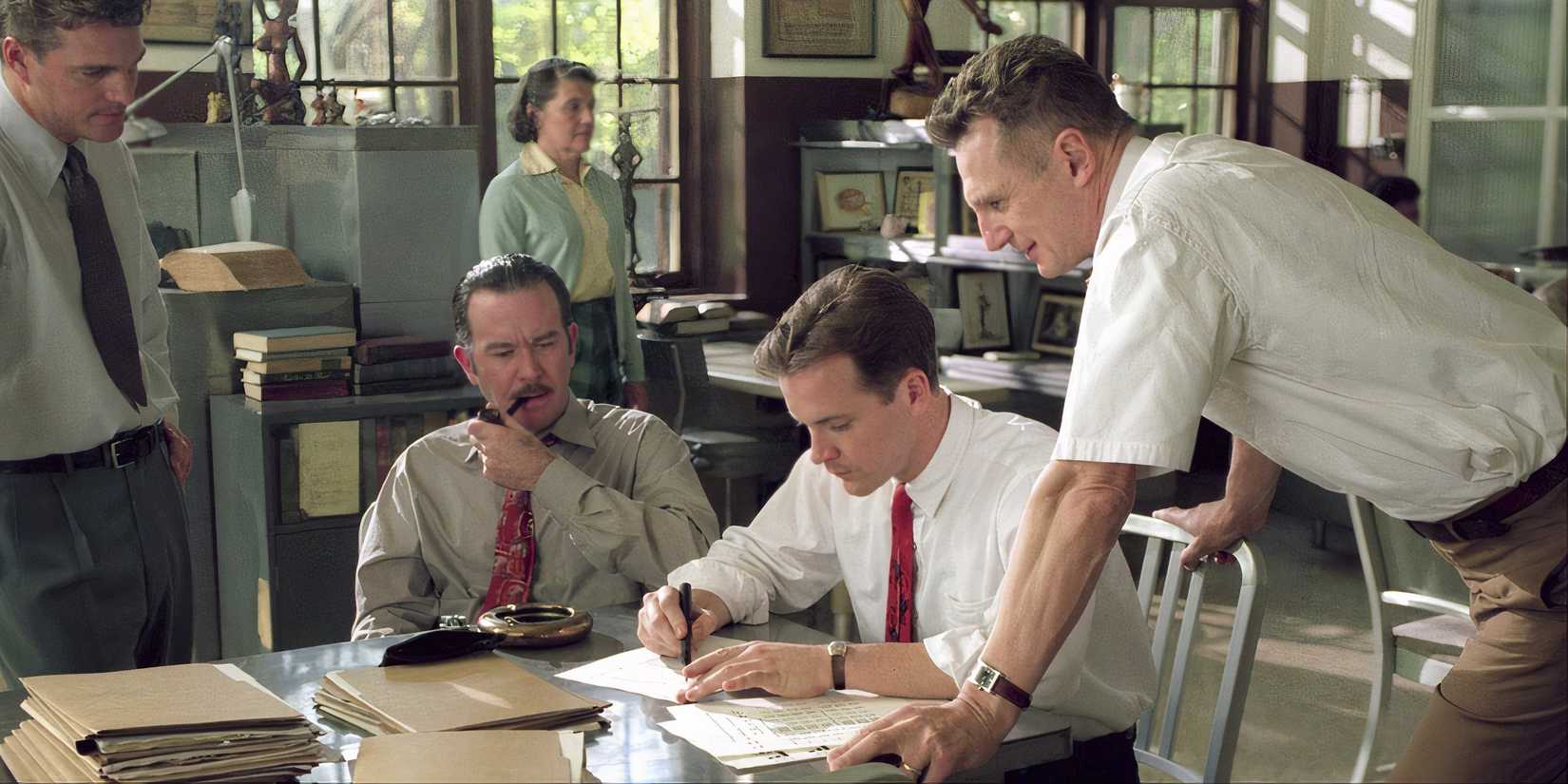 Peter Sarsgaard writing something while Liam Neeson stands over him watching in Kinsey