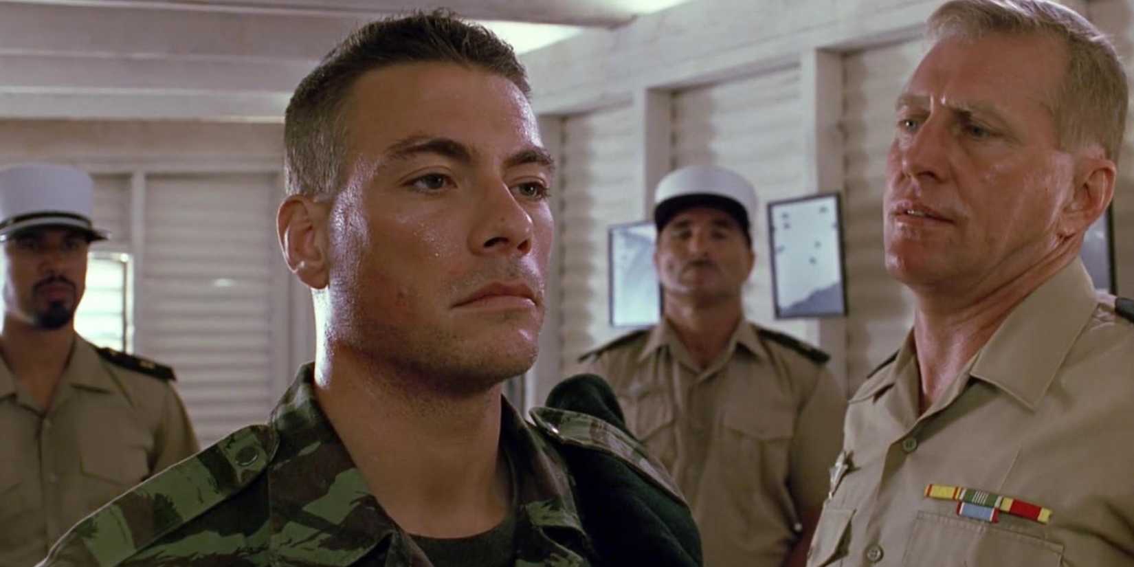 Jean-Claude Van Damme looking solemn in a soldier's fatigues as an officer talks to him in Lionheart