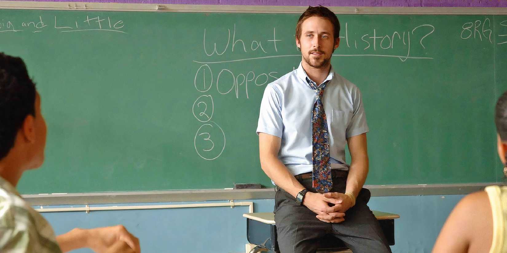 Ryan Gosling as Dan Dunne in Half Nelson sitting on his desk in a classroom.