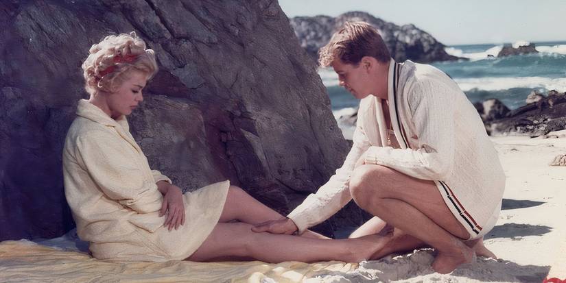 Johnny touches Molly's leg while the pair sit on a beach in A Summer Place (1959)
