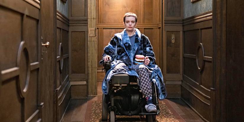Ruth Codd as Anya, in a blue robe, sitting in a wheelchair and holding a donut-shaped mug in 'The Midnight Club.'