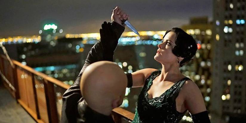 Jane fighting off a man who is trying to pierce a spear into her face. Both of them are standing dangerously near the railing of a rooftop.