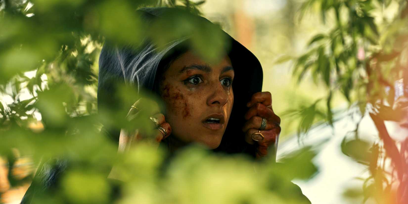 Rhianne Barreto as Rani hiding among the bushes in a black hoodie in Season 3 of The Outlaws