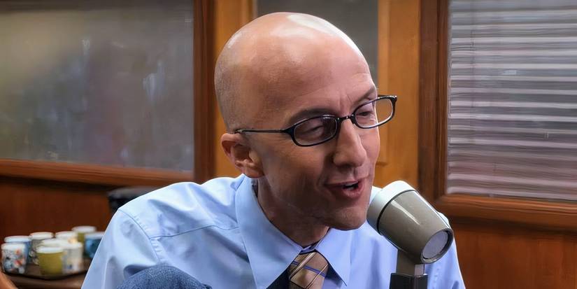 A still from Community of Dean Pelton, played by actor Jim Rash, speaking into a PA Microphone.