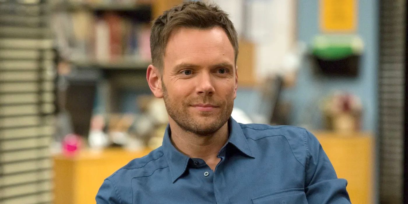 Joel McHale wears a blue shirt and smirks in the study room as Jeff Winger in Community.
