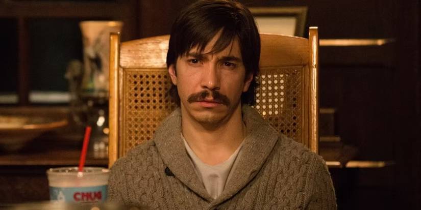Justin Long duduk di kursi dan melihat ke depan dengan ekspresi frustrasi di Tusk.