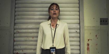 Maika Monroe stands with her back against a blood-spattered wall with her FBI badge around her neck, afraid