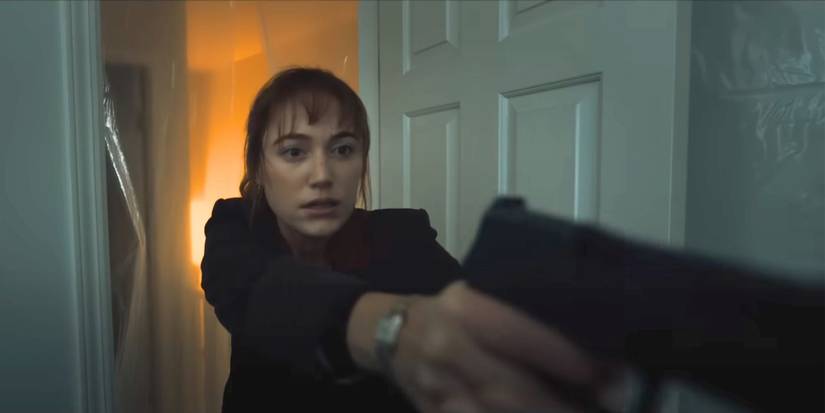 Maika Monroe pointing a gun while walking through the door in Longlegs.