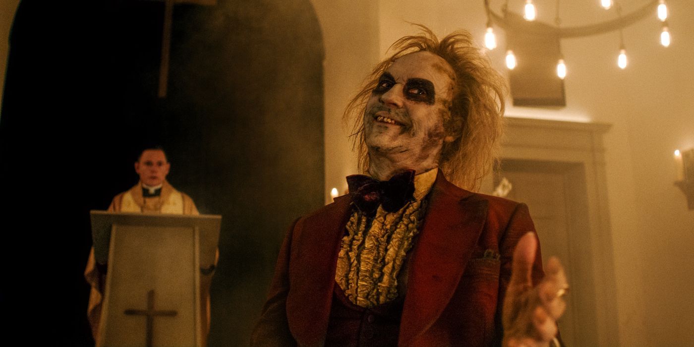 Beetlejuice wearing a red tux and pointing at someone off-camera in Beetlejuice Beetlejuice.
