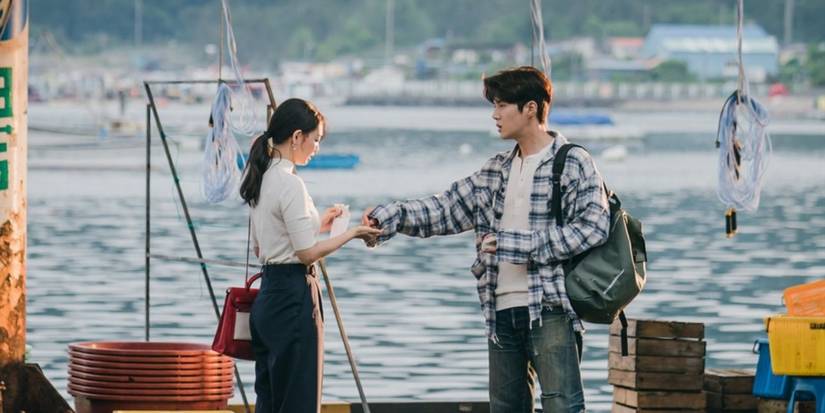 Shin Min-a and Seok-ho exchange something at a fishing port with an ocean backdrop in Hometown Cha Cha Cha.