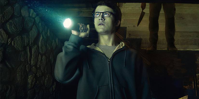Logan shines a flashlight in a dark room as a shadowy, knife-wielding figure appears behind him