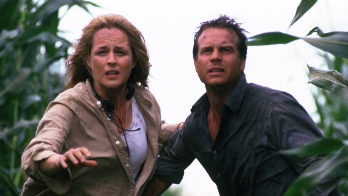Jo (Helen Hunt) and Bill Harding (Bill Paxton) standing in a corn field staring ahead with concerned expressions and Jo reaching her hand forward in Twister