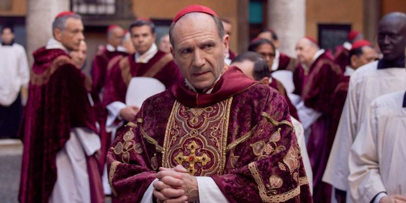 Ralph Fiennes as Cardinal Thomas Lawrence wears papal finery while walking away from men in similar attire in Conclave. 
