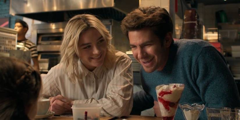Florence Pugh and Andrew Garfield laughing while sitting next to each at a booth in an ice cream shop in We Live in Time.