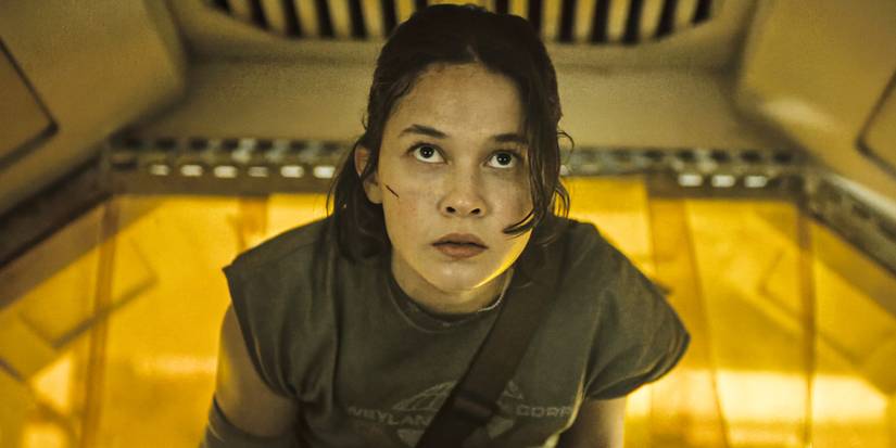 Cailee Spaeny walking through a yellow tinted spaceship looking up in Alien-Romulus