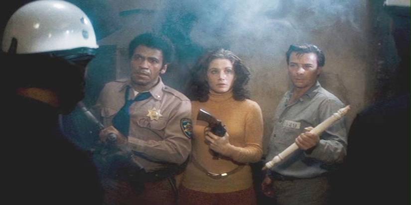 Two men and a woman against a wall looking at two cops with their backs to the camera in Assault on Precinct 13