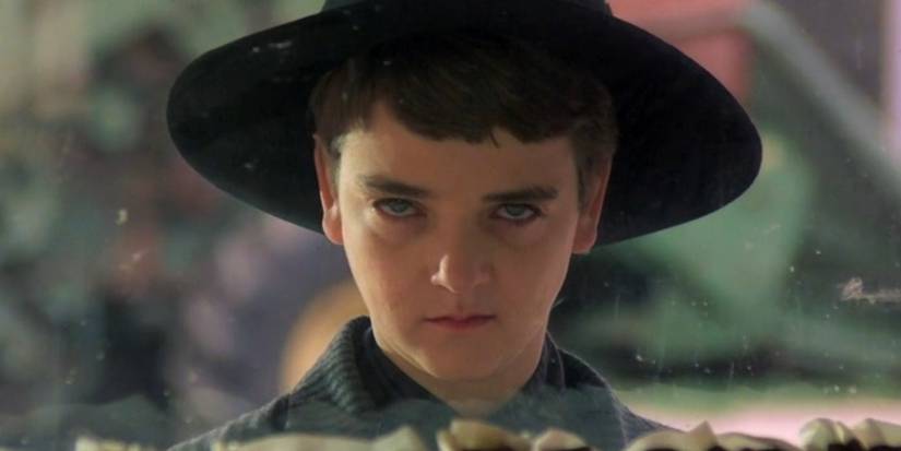 Isaac (John Franklin) in a black hat and suit stares through a window in Children of the Corn, 1984.