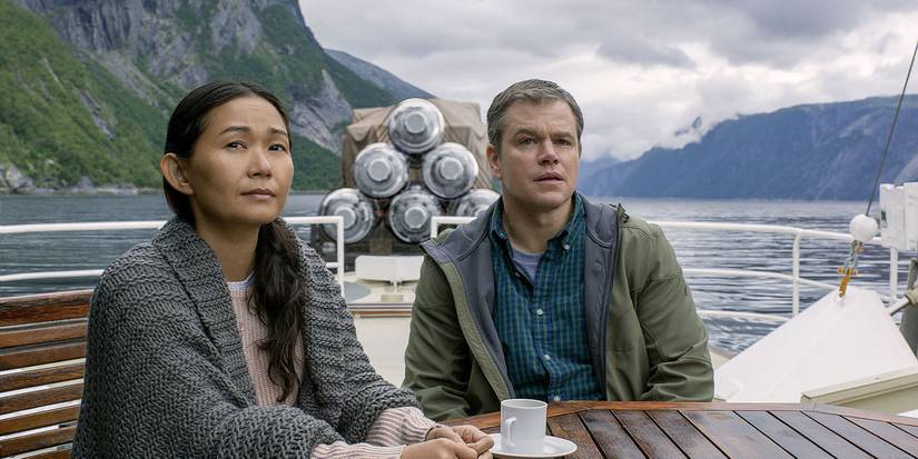 Hong Chau and Matt Damon sitting at a table on a boat on a lake looking up off-camera