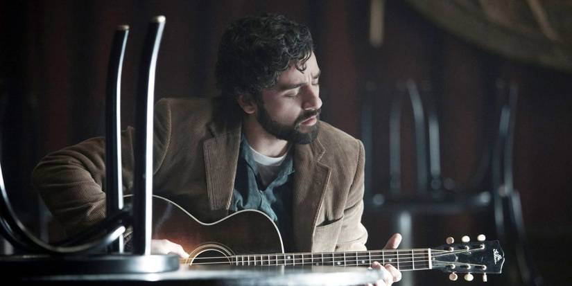 Oscar Isaac as Llewyn Davis playing an acoustic guitar in Inside Llewyn Davis.
