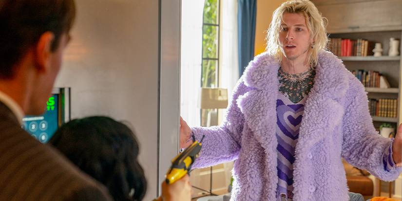 Machine Gun Kelly holding out his arms in a purple coat in a doorway