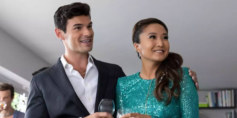 Ashley Park dan Paul Foreman berdiri bersebelahan sambil memegang gelas anggur di 'Emily in Paris' Musim 3.