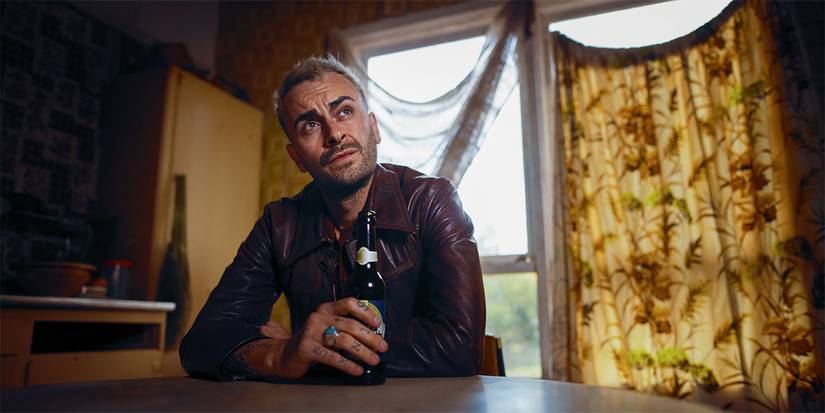 Joe Gilgun as Cassidy with a bottle of beer and sitting at a table in Preacher