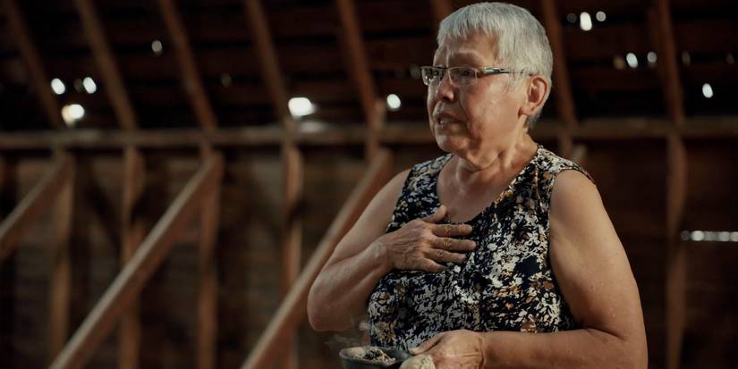 A woman holds her hand to her chest and cries in a dark barn in the 2024 documentary, Sugarcane