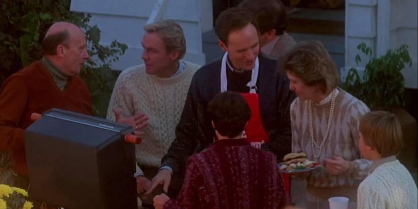 Terry O'Quinn as Jerry Blake wearing an apron and using a grill in a backyard surrounded by neighbors in 'The Stepfather' (1987).