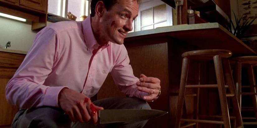 Terry O'Quinn as Jerry Blake crouching down while holding a bloodstained knife in a kitchen in 'The Stepfather' (1987).