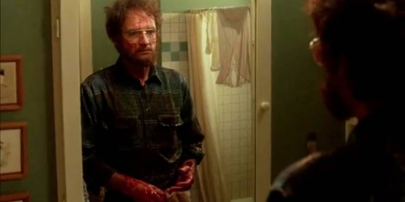 Terry O'Quinn as Jerry Blake with a beard and glasses and covered in blood, staring into a mirror in 'The Stepfather' (1987).